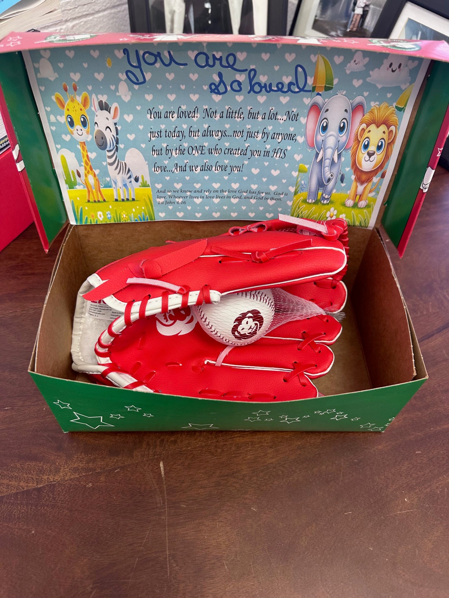 Red baseball glove and ball in a box with a children's book on a wooden surface
