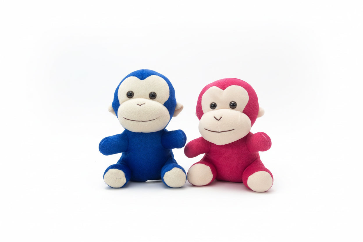 Two monkey plush toys, one red and one blue, on a wooden surface.