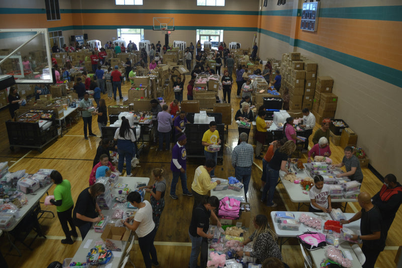 Group of people sorting items in a large indoor space with tables and boxes.