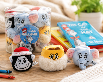 A Dr. Seuss-themed plush toy set displayed on a wooden table, featuring a clear jar filled with plush characters and three individual plush toys in front: a black-and-white monkey wearing a red Santa hat, a yellow-and-white cat face, and a light blue elephant.