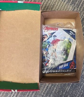 Open cardboard box with a plastic-wrapped toy on a textured carpet