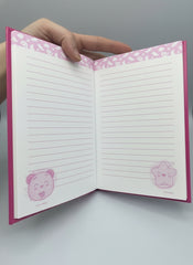 Notebook with pink decorative edges and lined pages held by a hand.