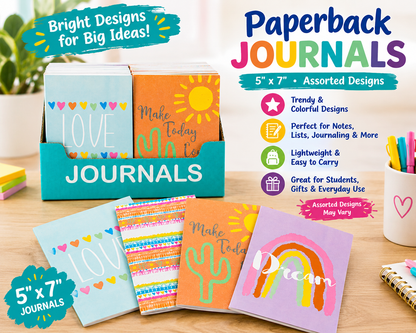A retail display of assorted 5x7 Paperback Journals on a wooden desk, featuring colorful covers with designs like a sun, cactus, and rainbow. The display includes a teal cardboard stand, a promotional badge, and a list of product features on the right.